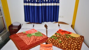 A bed with two blankets, a nightstand, a lamp, and a window with curtains. - binay chapa homestay Jaldapara wildlife sanctuary best leving accommodation  (Madhya Madarihat)