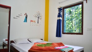 A single bed with a white mattress and a red blanket, a wooden headboard, a window with blue curtains, and a wall with a couple kissing and a tree with leaves. - binay chapa homestay Jaldapara wildlife sanctuary best leving accommodation  (Madhya Madarihat)