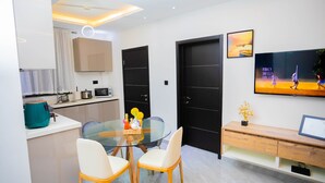 A modern kitchen with a glass dining table, two chairs, and a wooden cabinet.