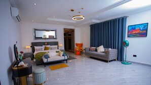 A modern hotel room with a bed, a sofa, a desk, and a standing fan.