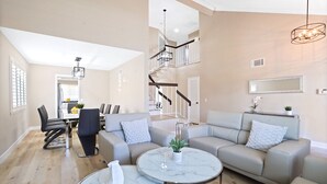 A spacious living area with a modern staircase, a dining area with a table and chairs, and a seating area with two sofas and a coffee table. - Spacious Clean Home w/ Quality Furniture close to Disneyland & Huntington Beach! (Garden Grove)