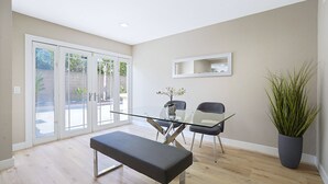 A modern dining area with a glass table, two chairs, a bench, a potted plant, and a large mirror on the wall. - Spacious Clean Home w/ Quality Furniture close to Disneyland & Huntington Beach! (Garden Grove)