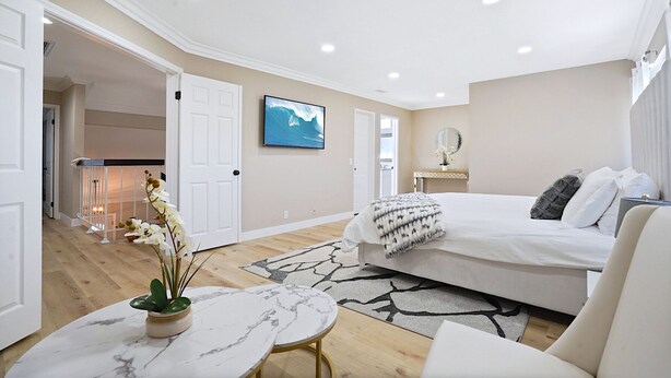 A modern bedroom with a large bed, a TV, and a small table with a plant. - Spacious Clean Home w/ Quality Furniture close to Disneyland & Huntington Beach! (Garden Grove)