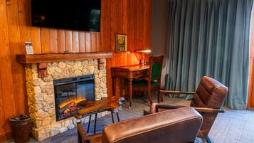 A cozy room with a stone fireplace, leather seating, a flat-screen TV mounted above the fireplace, and a wooden wall.