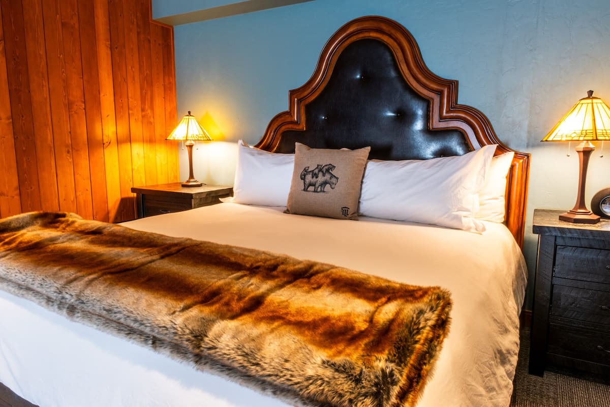 Een bed met een houten hoofdbord, twee bedlampen, een vachtkleed en een kussen met een bergleuk.