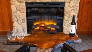 A stone fireplace with a fire, a bottle of wine, and two glasses on a wooden table. - Mount Lemmon Lodge (Mount Lemmon)