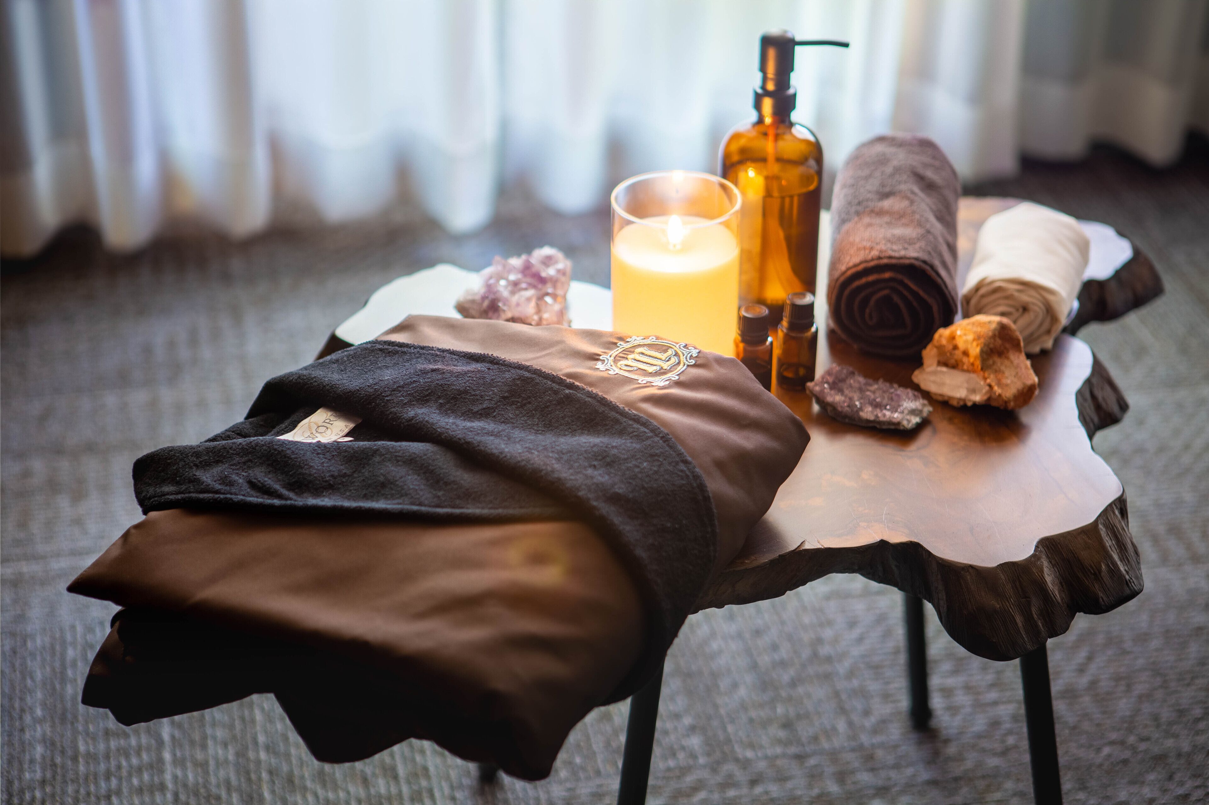 A spa setting with a towel, candle, and essential oils on a wooden table.