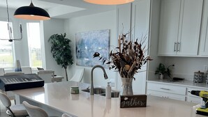 Una cocina moderna con una isla grande, taburetes de bar, luces colgantes y una planta en maceta.