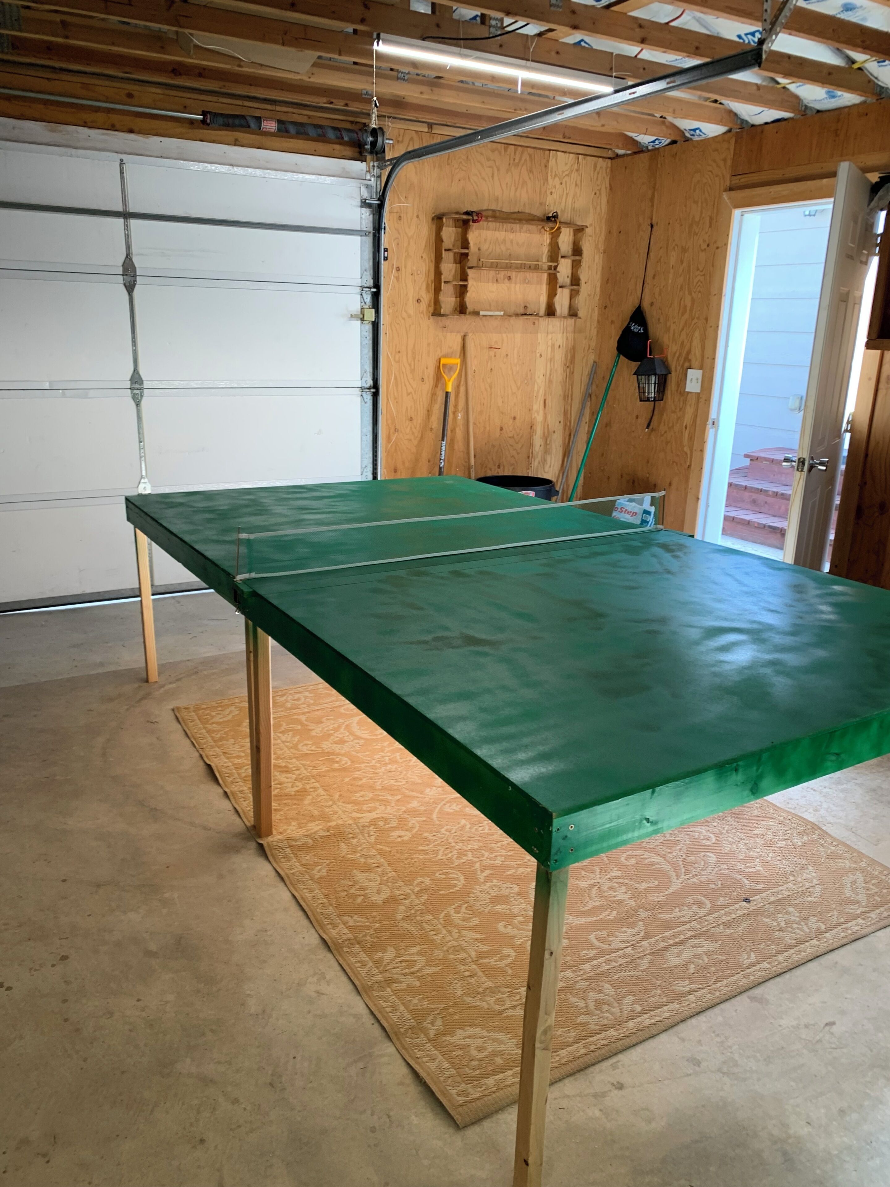 A garage with a green table, wooden walls, a concrete floor, and a garage door.