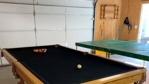 Una mesa de billar con bolas, una mesa de ping pong verde y un techo de madera.