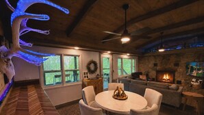 Una sala de estar acogedora con chimenea, un comedor con una mesa redonda y sillas, y una amplia escalera de madera.