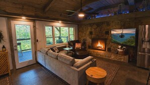 Una sala de estar acogedora con chimenea de piedra, un sofá, un televisor y un ventilador de techo.