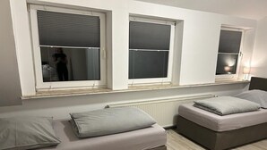 A room with two beds, each with a pillow and a blanket, and three windows with blinds. - Wohnen wie zu Hause (Löhne)