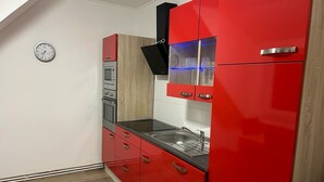 A kitchen with red cabinets, a black range hood, and a stainless steel sink. - Wohnen wie zu Hause (Löhne)