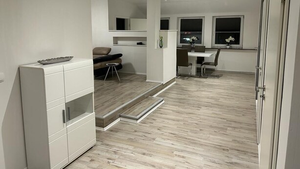 A modern kitchen with white cabinetry, a dining area with a table and chairs, and a staircase leading to an upper level. - Wohnen wie zu Hause (Löhne)