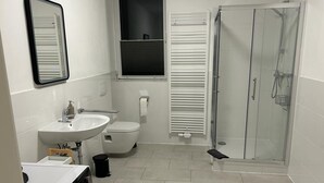 A modern bathroom with a white sink, toilet, and glass shower enclosure. - Wohnen wie zu Hause (Löhne)