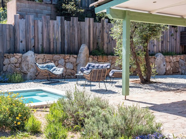 Un patio con sillas de mimbre, una piscina pequeña y un muro de piedra.