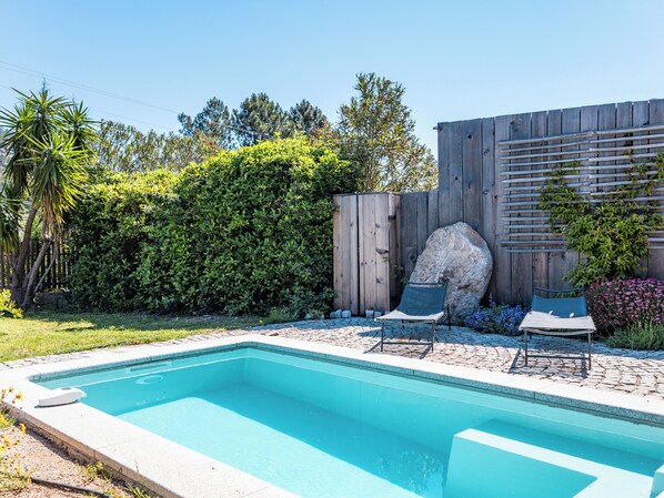 A rectangular swimming pool with two lounge chairs and a wooden fence in the background.