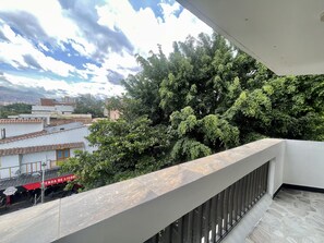 Ein Balkon mit Blick auf einen dichten, grünen Baum und ein Gebäude mit dem Schild 'ENDA DE LICOR'.