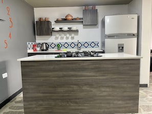 Eine moderne Küche mit einer zentralen Kochinsel, eingebauten Regalen über der Arbeitsplatte und einem Kühlschrank zur Rechten.
