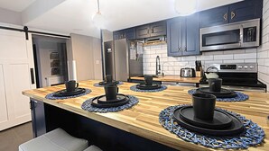 Een moderne keuken met donkere kastjes, een roestvrijstalen koelkast, een magnetron en een houten kookeiland met zwarte mokken.