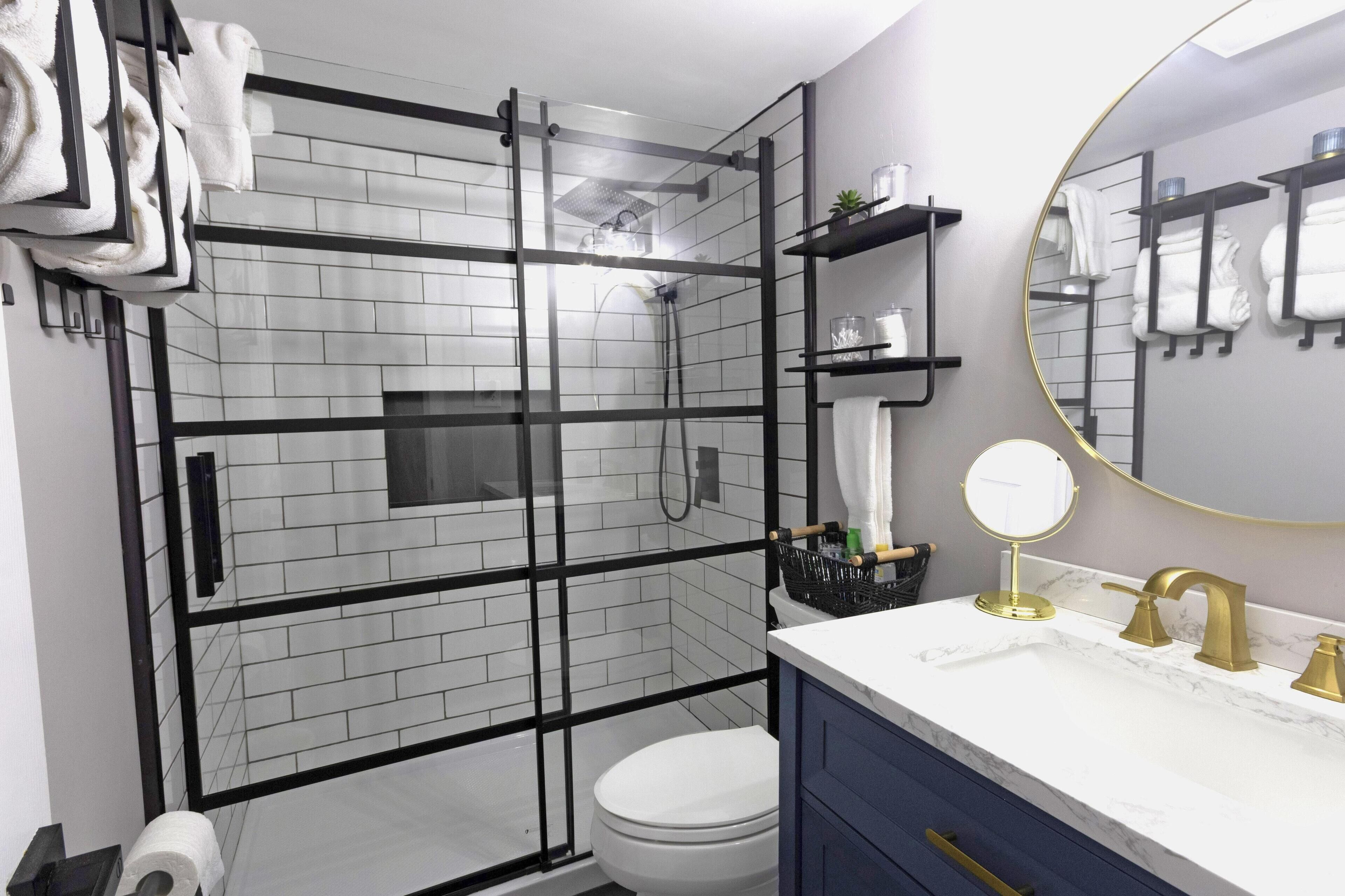 A modern bathroom with a glass-enclosed shower, a white toilet, a marble sink with gold fixtures, and a large mirror.