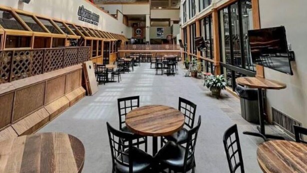 Een ruime binnenruimte met hoge plafonds, grote ramen en diverse zithoeken, waaronder tafels en stoelen.