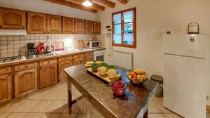 A kitchen with wooden cabinets, a microwave, a refrigerator, and a fruit bowl on the counter.