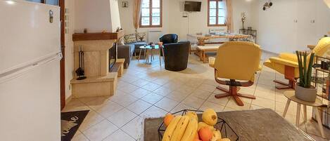 A spacious living area with a dining table, chairs, and a fruit basket.