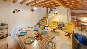 A spacious living area with a dining table set for six, a staircase leading to an upper level, and a kitchen area with wooden cabinets.