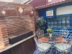 A brick barbecue grill, outdoor seating with metal chairs, and a blue window with a grid pattern. - 5 de Mayo Boutique Loft (Tijuana)