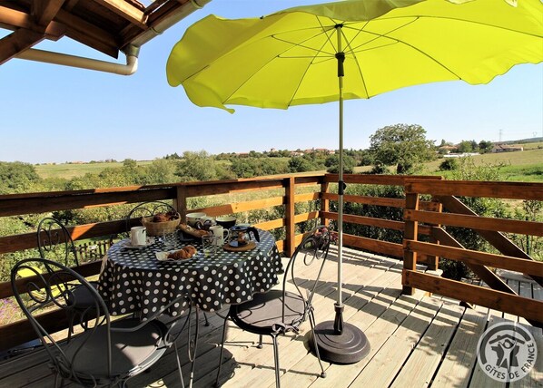 Een houten terras met een tafel, stoelen, een parasol en uitzicht op het platteland.