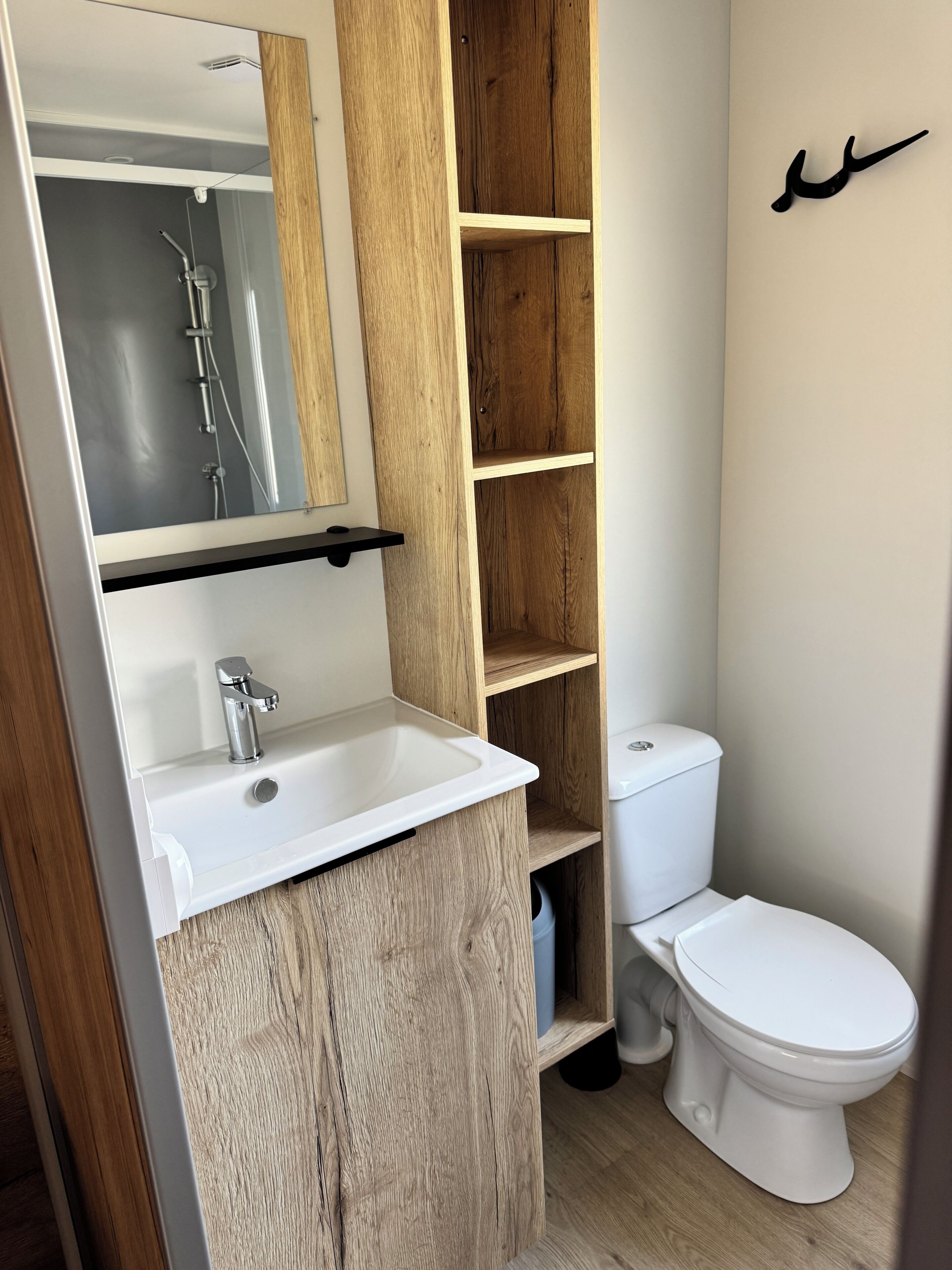 Une salle de bain avec un meuble-lavabo en bois, un miroir, un lavabo blanc, des toilettes et une étagère.