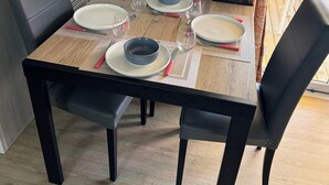 A dining table set with plates, bowls, and glasses, surrounded by black chairs, with a wooden floor and a view of outdoor furniture.