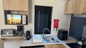 A compact kitchen with a dishwasher, a coffee maker, a kettle, and a toaster.