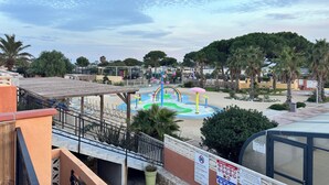 A playground with slides and a water feature, surrounded by palm trees and a covered seating area.