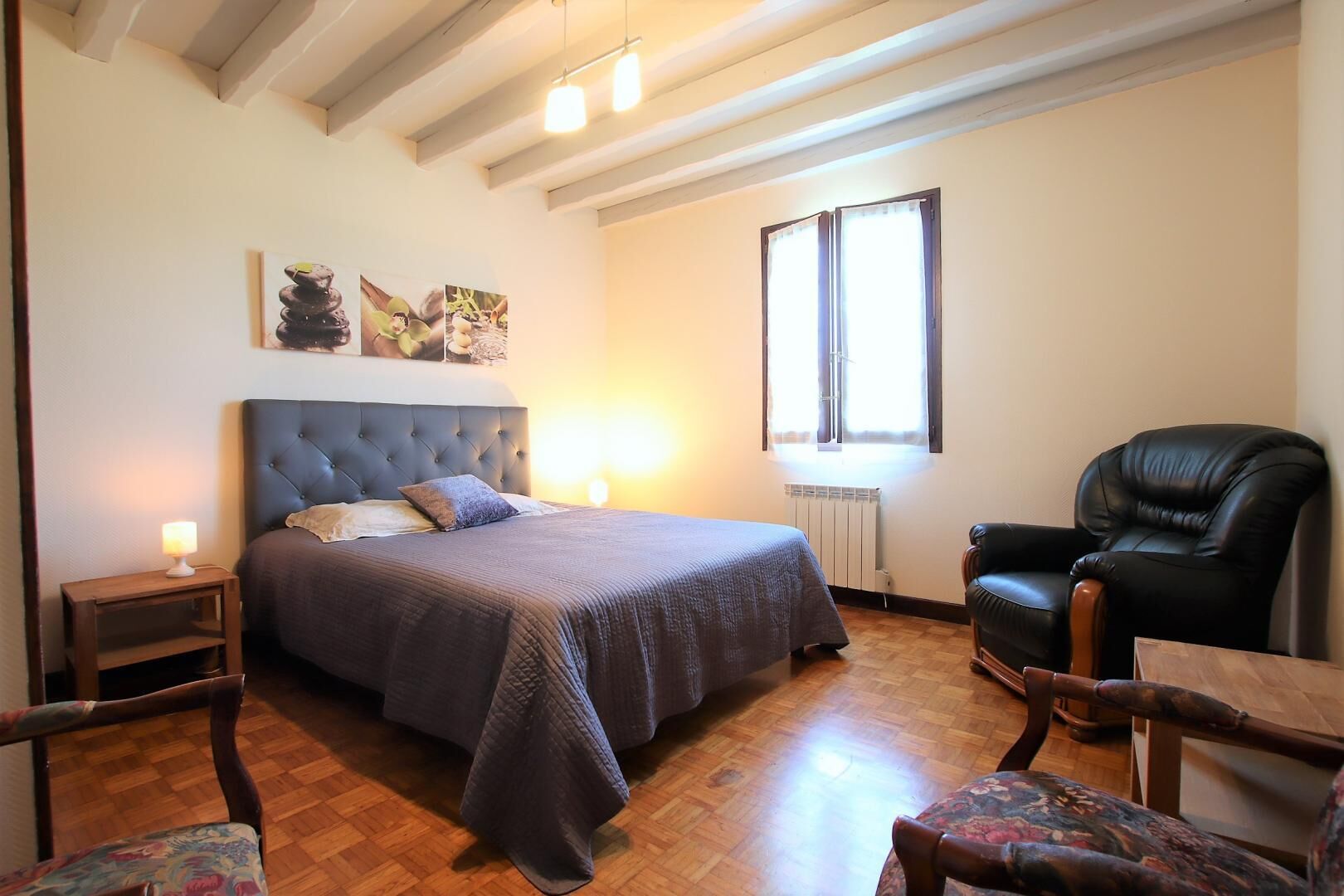 Une chambre à coucher avec un grand lit, une chaise, une petite table et une fenêtre.