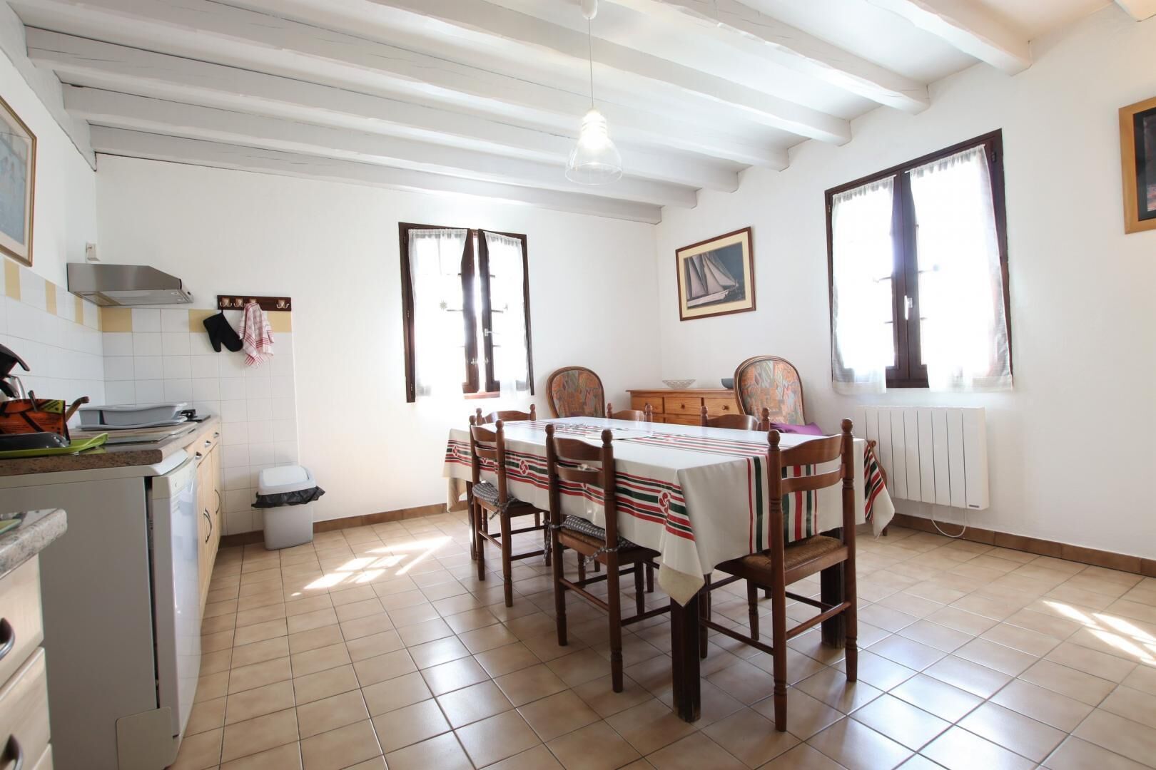 A dining area with a table set for four, wooden chairs, a white tablecloth, and a window with curtains.