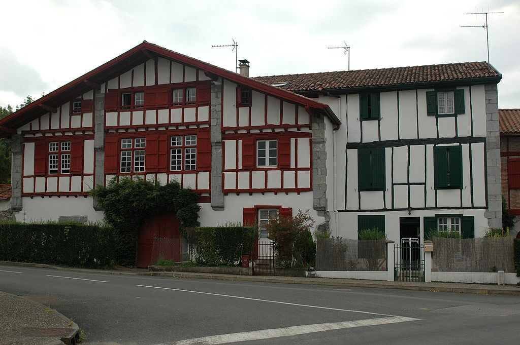 Una casa tradicional de entramado de madera con fachada roja y blanca, una entrada con portón y un camino de acceso pavimentado.