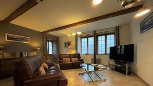 A living room with a brown leather sofa, a glass coffee table, a television, and large windows. - APEZAINEA - SARE - Gîte (SARE)