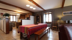 A dining area with a wooden table and bench, kitchen cabinets, and a window with curtains. - APEZAINEA - SARE - Gîte (SARE)