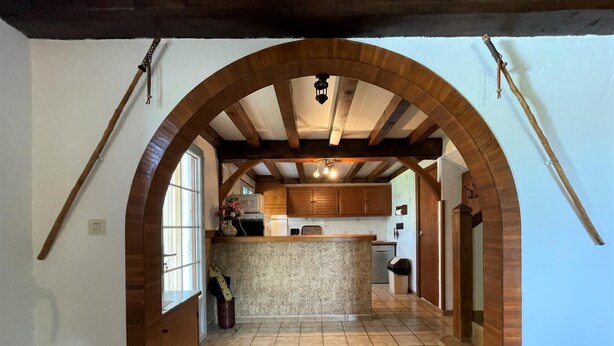 Una cocina con techo abovedado, vigas de madera, una isla central y suelo de baldosas.