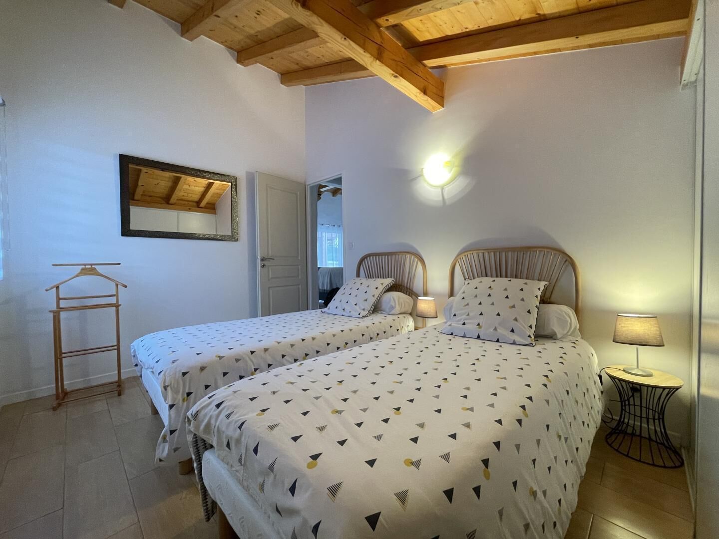 A bedroom with two beds, a wooden ceiling, a mirror, and a small table with a lamp.