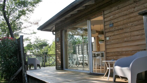 Eine Holzhütte mit einer Terrasse, eine Glastür führt zu einem Patio mit Gartenmöbeln.