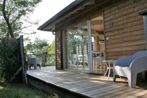 Eine Holzhütte mit einer Terrasse, eine Glastür führt zu einem Patio mit Gartenmöbeln.