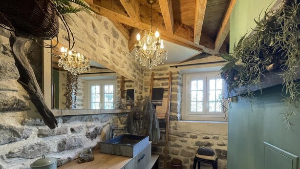 A rustic bathroom with stone walls, a wooden vanity, a sink, and a chandelier. - Maison Mado-lily - Bidos (BIDOS)