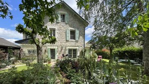 A stone house with green shutters, a garden with various plants and flowers, and a paved pathway leading to the entrance. - Maison Mado-lily - Bidos (BIDOS)