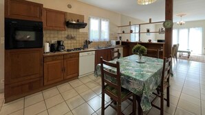 A kitchen with wooden cabinets, a microwave, a sink, and a dining table with chairs. - CHEZ LABAT 2 - ESPOEY (ESPOEY)