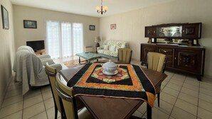 A living room with a sofa, a dining table with a quilt, a TV, and a cabinet. - CHEZ LABAT 2 - ESPOEY (ESPOEY)