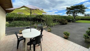 An outdoor patio with a table and chairs, a yellow umbrella, and a garden with various plants and a tree. - CHEZ LABAT 2 - ESPOEY (ESPOEY)